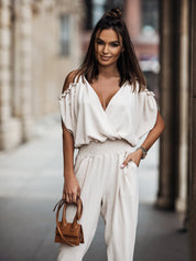 Witte jumpsuit met trendy open schouders, elegante overslag, v-hals en comfortabele elastische taille voor een veelzijdige en modieuze look, geschikt voor diverse gelegenheden.